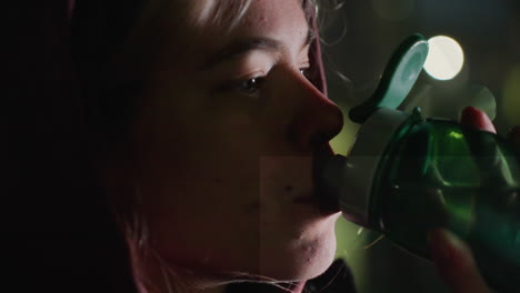 female athlete sipping water from transparent sports bottle under blurred city lights at twilight while hydrating after intense workout outdoors on urban bench for refreshing recovery moment