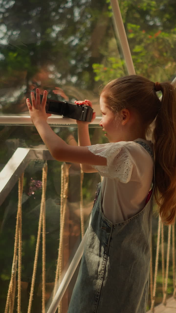 Child record video of nature at glamping. Little girl with camera shoots forest scene at eco hotel. Kid plays videographer on summer vacation