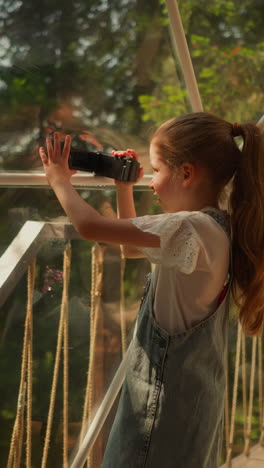 child record video of nature at glamping. little girl with camera shoots forest scene at eco hotel. kid plays videographer on summer vacation