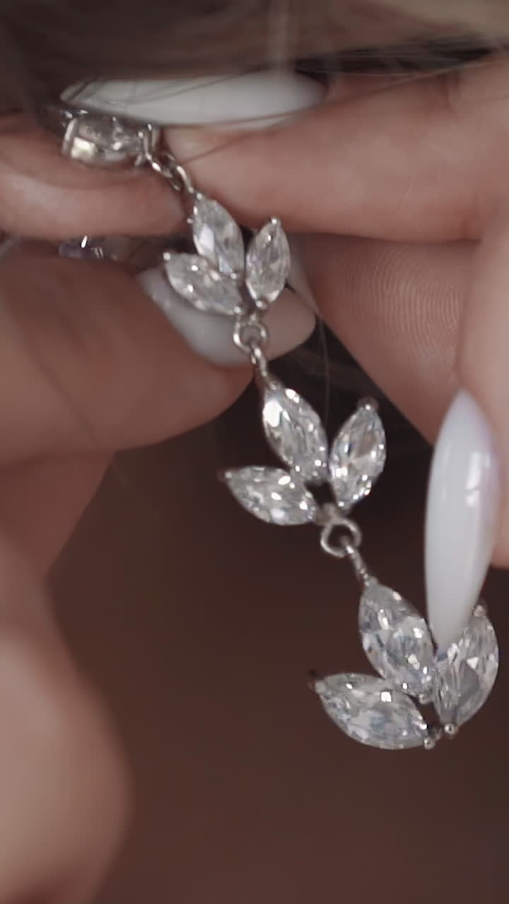 Woman with white manicure puts on silver floral style earring with shiny gems in ear in light room extreme close view. Expensive jewelry for ladies