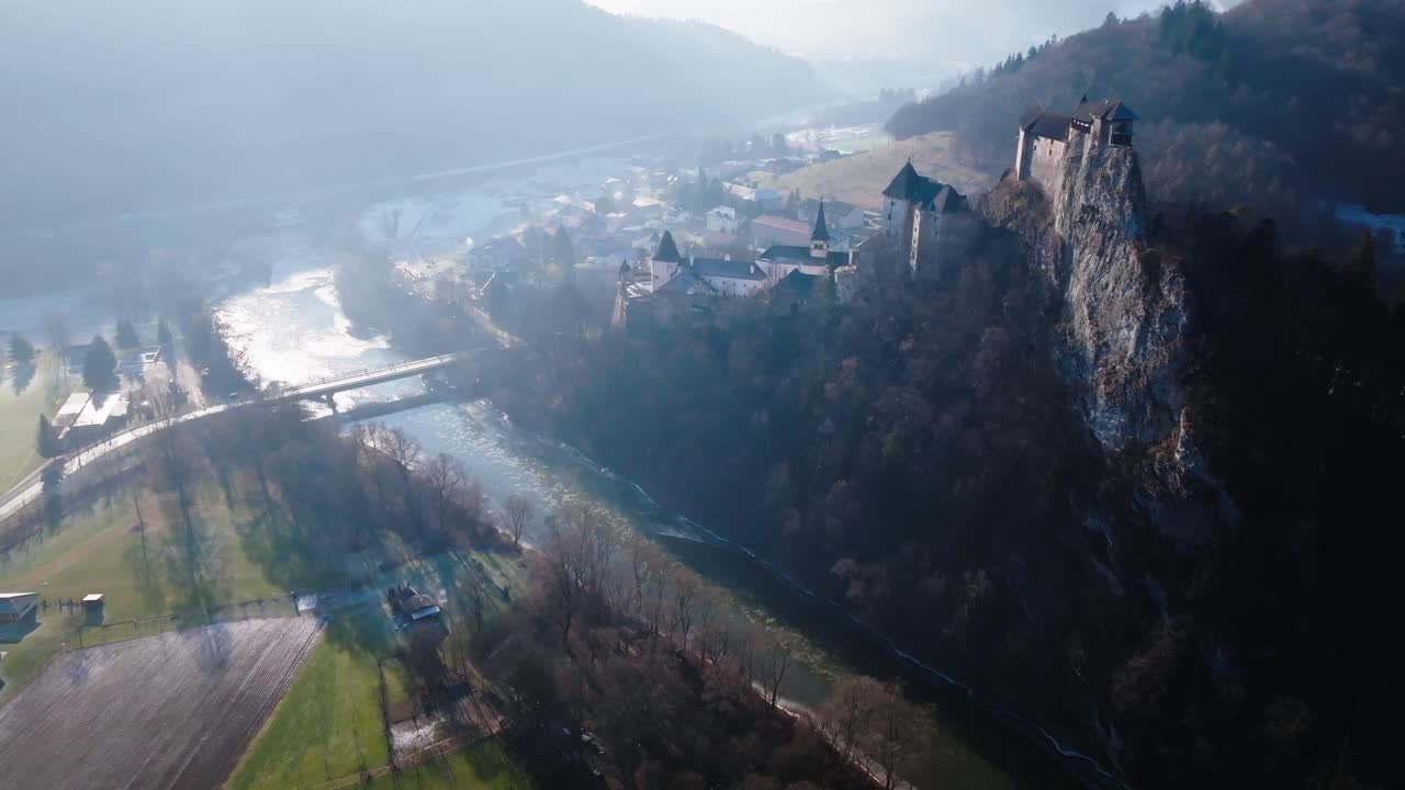 Drone footage of Orava Castle, a historic gem resting on a cliff, surrounded by lush hills, dense forests, and a winding river under a bright blue sky. (4K)
