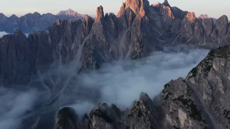 la inclinación hacia arriba del dron revela picos escarpados de cadini di misurina iluminados por el amanecer con inversión de nubes en el valle: vistas cinematográficas en los alpes dolomitas, italia