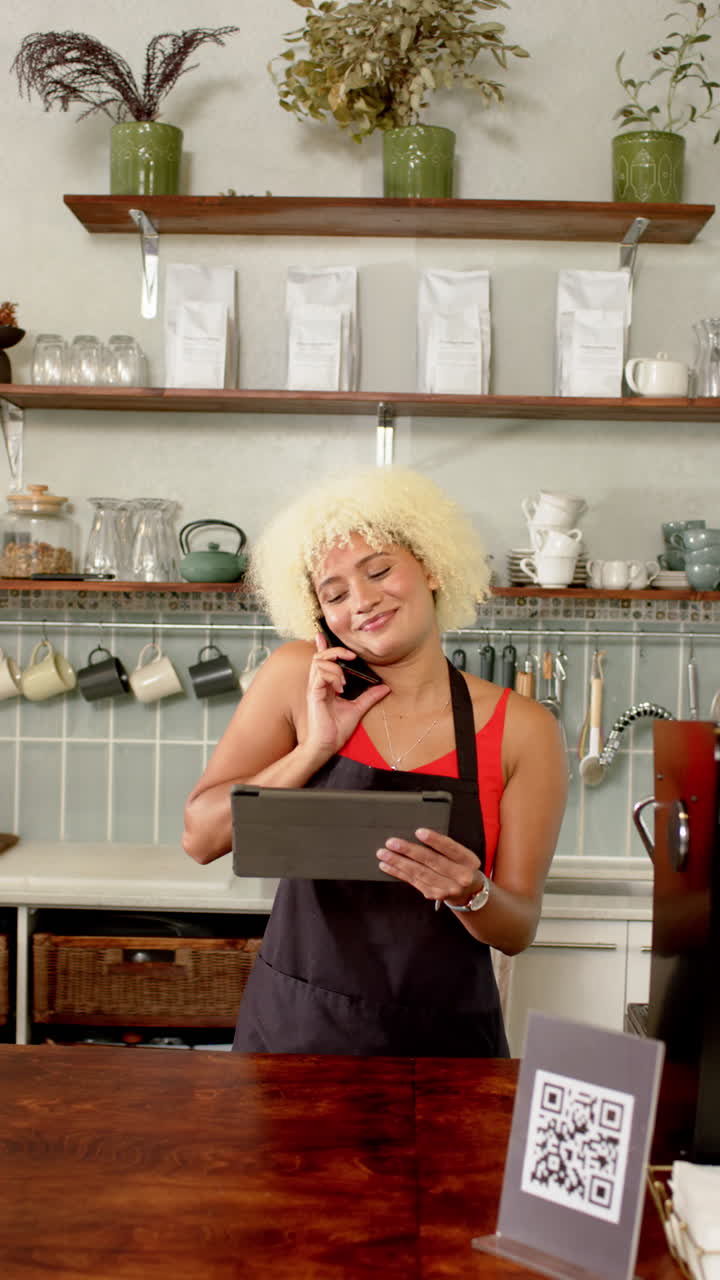 Vertical video: Talking on smartphone, barista holding tablet in cozy cafe setting