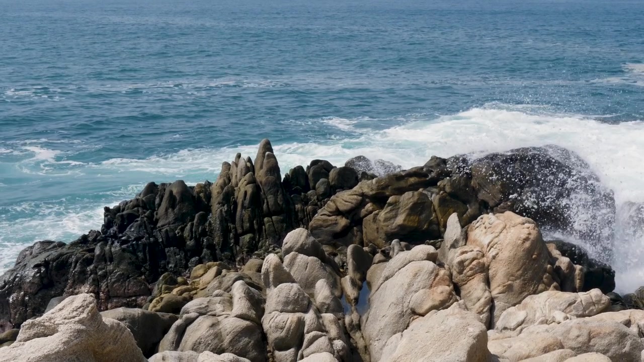 Slowmotion-landskab af havvandbølger, der sprøjter op over klipper og sten på kystlinjen, et forbjerg, en sandstrand og en bugt i Puerto Escondido, Mexico, Mellemamerika, rejseturisme