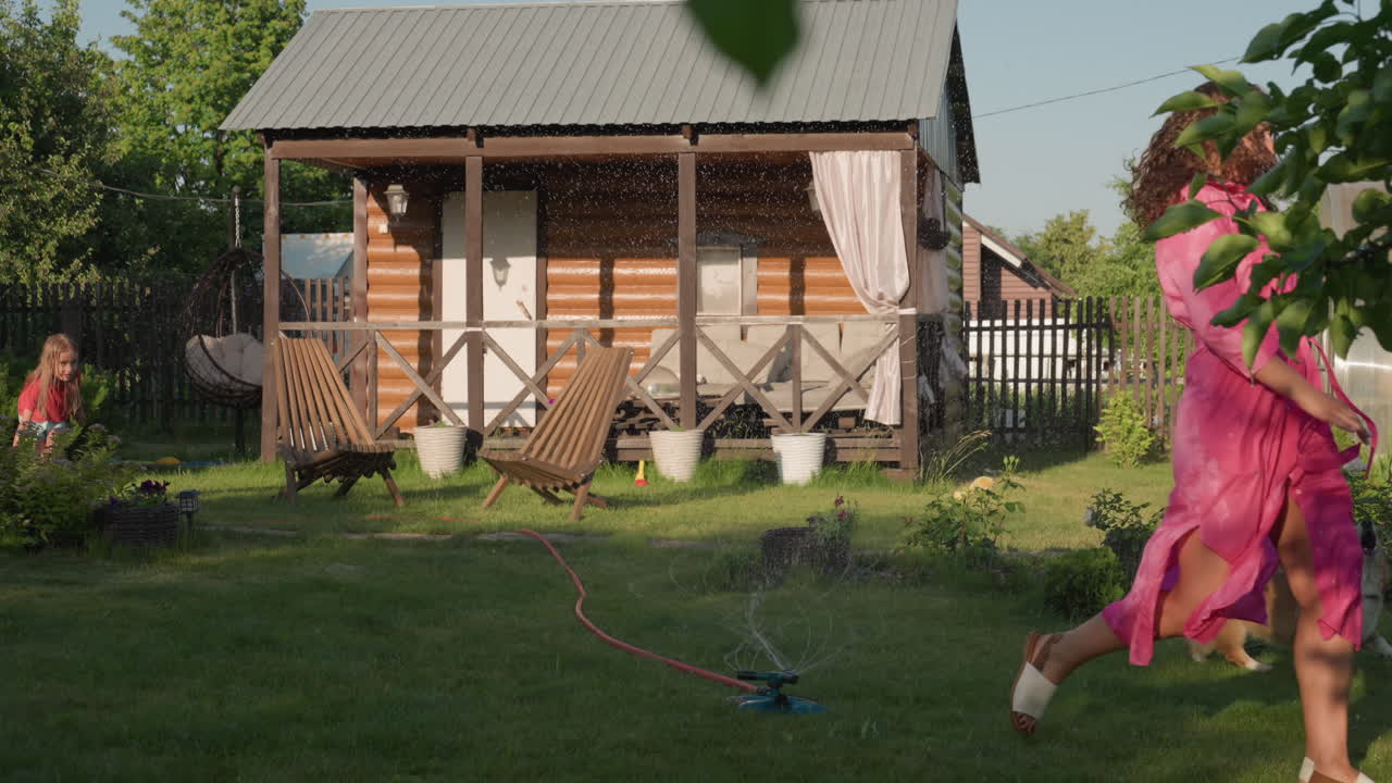 Woman And Child Playing Outside Together, Mother And Daughter Enjoy Yard Activities With Pet And Water, Family Members Share Joyful Outdoor Moments With Furry Pet And Playful Water Activities