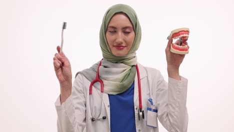 female dentist with hijab demonstrating dental care with a jaw model and toothbrush