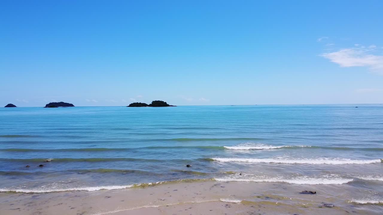 공중:드론이 배경에 섬이 있는 맑고 편안한 해안 바다의 파도 위로 뒤로 이동하고 있습니다.