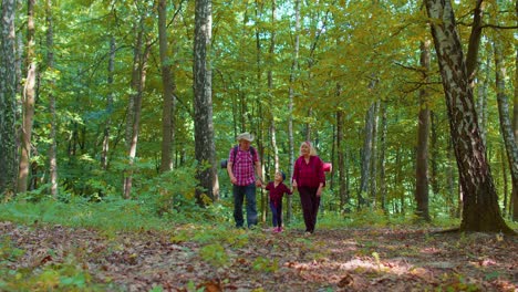 Senior-tourists-grandmother,-grandfather,-granddaughter-kid-talking,-walking-with-backpacks-in-wood