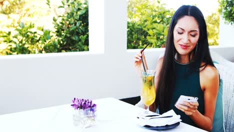 mujer hermosa usando teléfono móvil mientras bebe un cocktail