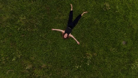 barefoot woman lying on grass field and looking up to the sky. aerial top down rising shot. brunette girl relax in nature.