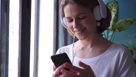 woman dancing while listening to music on cellphone by window