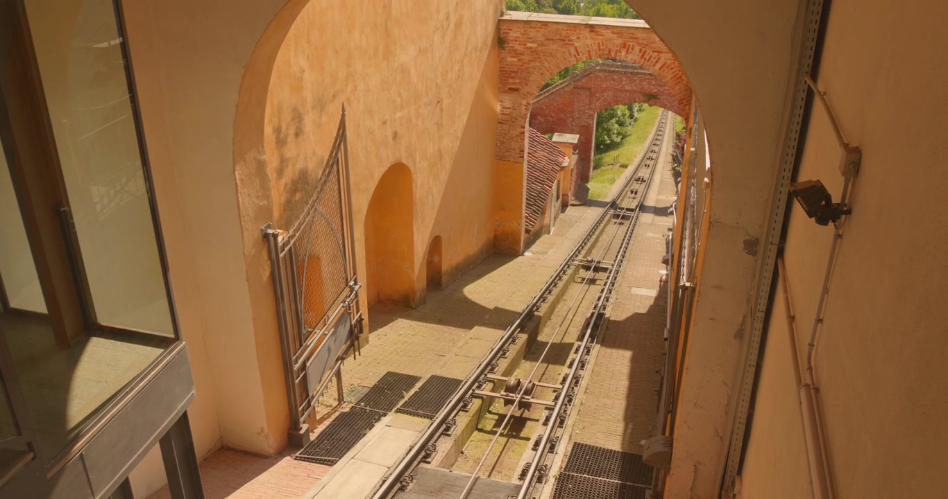 Binari storici della funicolare che attraversano un vecchio arco in pietra e un portale in mattoni durante una giornata luminosa a Mondovì, Piemonte, Italia.