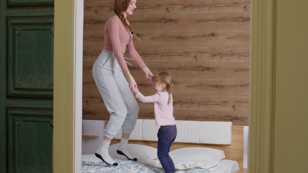 Happy funny family mother and child kid daughter dancing, jumping on bed, listening music at home