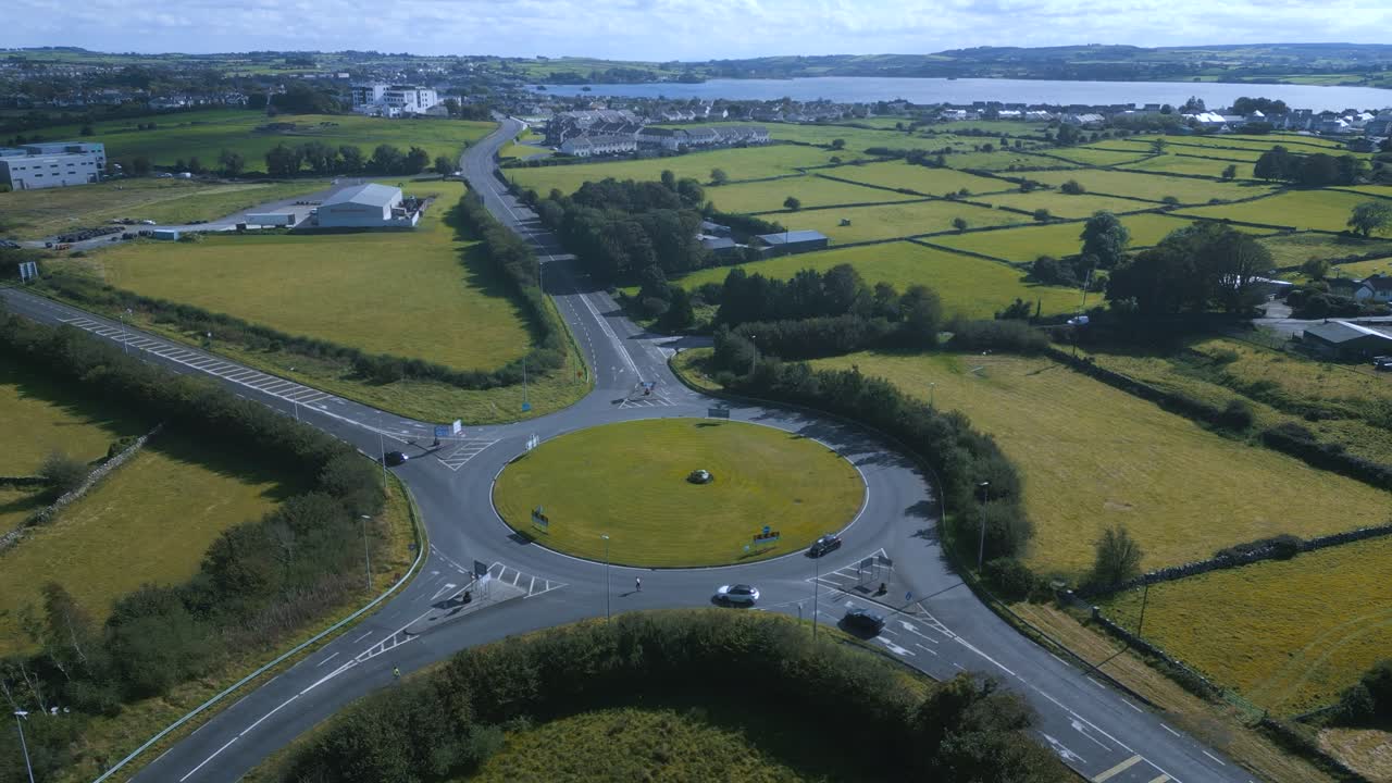 Drone footage of the Lake View Roundabout in Midleton, Ireland, connecting the N25 and R630 surrounded by green fields and a scenic lake background