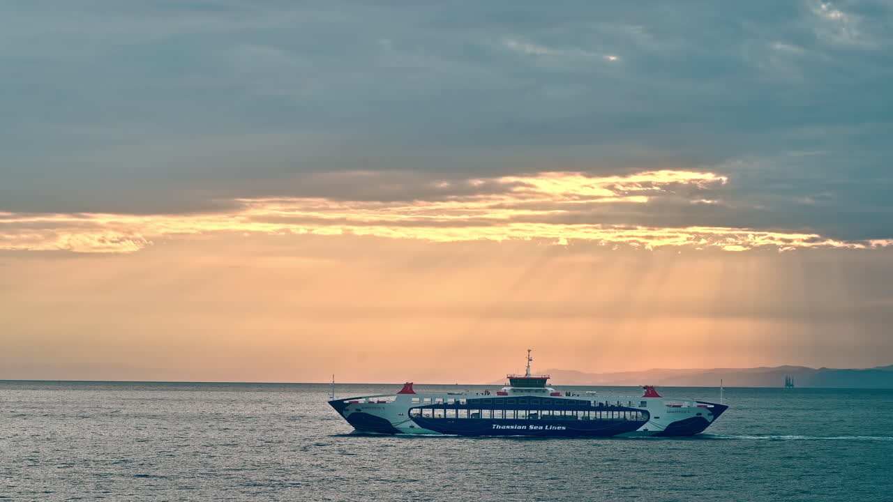 THASOS, GREECE - SEPTEMBER 23, 2020: View of sunset from the water of Aegean sea. Moving ferryboat. Orange sky, cloudy weather, godrays