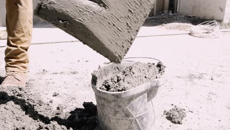 el trabajador saca cemento manualmente en un balde con una pala en el sitio de construcción