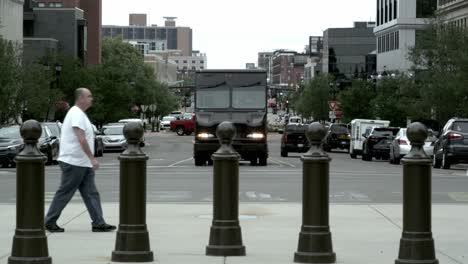 Middle-aged-Caucasian-male-in-jeans-and-white-t-shirt-walking-in-downtown-Lansing,-Michigan-with-Michigan-Avenue-in-the-background