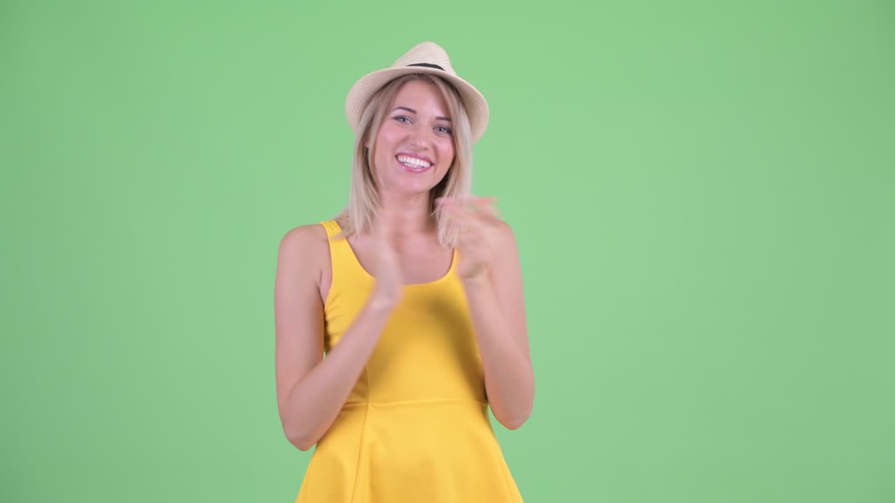 Studio shot of young tourist woman looking excited and clapping hands against green background