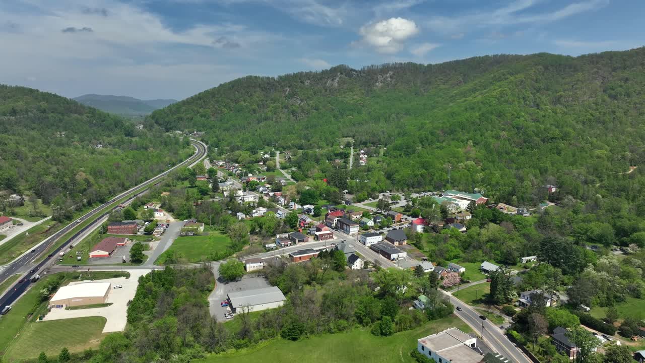 Lovingston City at highway with traffic in green mountains. Sunny day with blue sky in spring. Small town with houses and homes in Virginia. Aerial backwards Panorama wide shot.