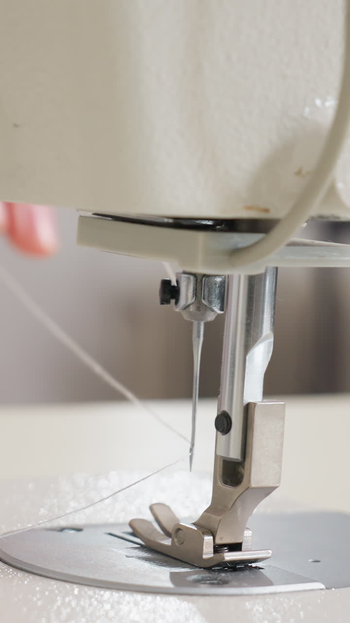 primer plano del pie de costura industrial y la aguja de la máquina de alta resistencia suspendidos sobre la tela, mecanismo de alimentación automática estable, iluminación neutra y fría, ambiente de producción en estudio de fábrica, costura de precisión