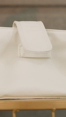hand of woman with neat manicure putting white leather handbag on table. high quality accessory for stylish outfit on blurred background closeup