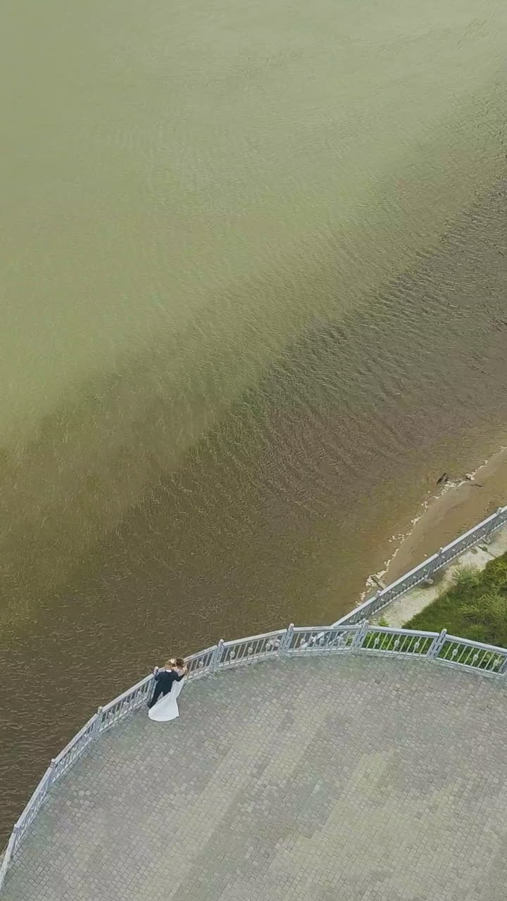 distant newly wedded bride and groom look at green tranquil river from viewpoint on autumn day aerial view