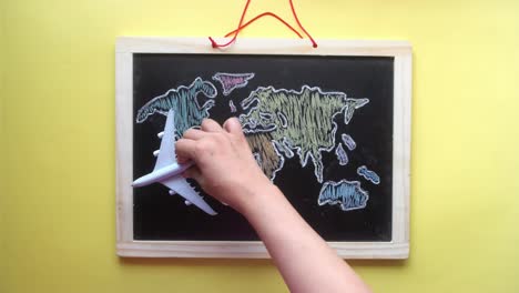 child's hand holding airplane over hand-drawn world map on chalkboard