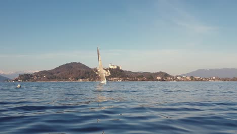 Zoom-De-ángulo-Bajo-Pov-De-Velero-Navegando-En-El-Lago-Maggiore-Con-Un-Castillo-De-Angrya-En-Segundo-Plano