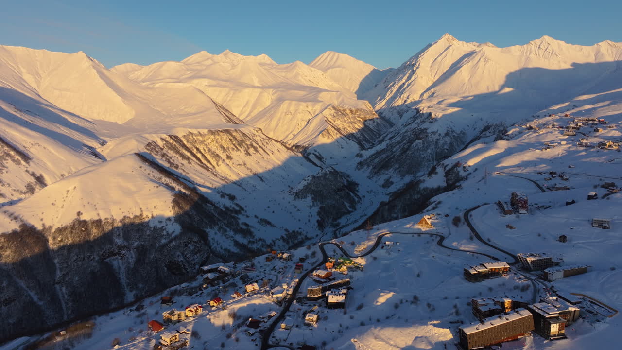 Filmato drone cinematografico in 4K che si libra sopra Gudauri all'ora d'oro, rivelando le vaste vette del Caucaso che risplendono nella calda luce dell'alba. Gudauri_135