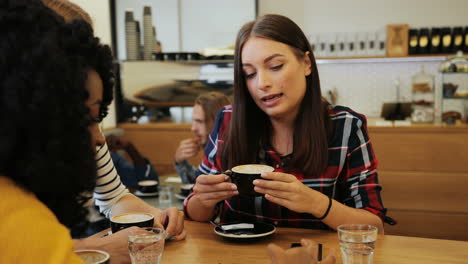 close-up view of african american and caucasian women friends talking and drinking coffee sitting at a table in a cafe