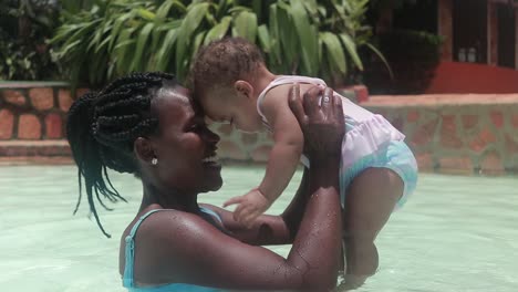 una mujer africana y su hija pequeña jugando juntos amorosamente en una piscina