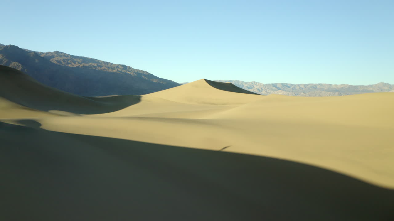 석양에 황금빛 모래 언덕을 날아다니는 드론 영상, 배경에 산이 있는 사막