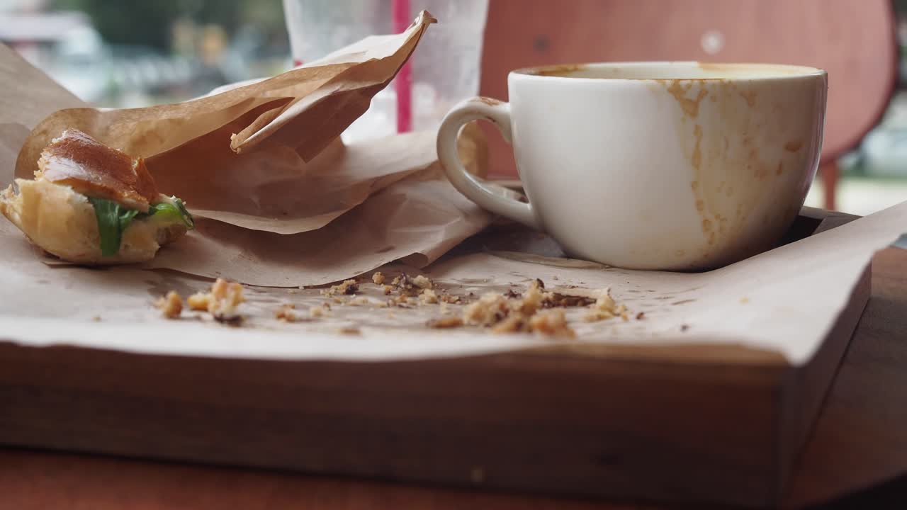 taza de café sucia y sobras de sándwich en una bandeja de madera