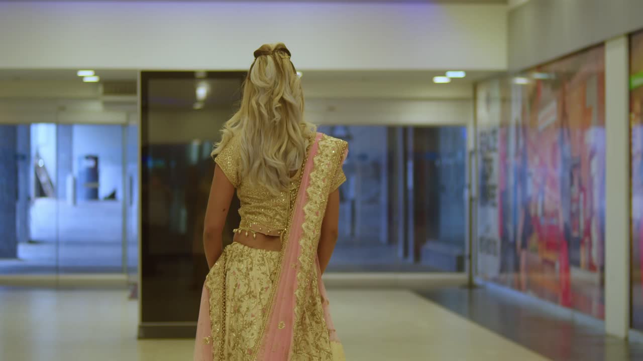 Uma jovem de ascendência indiana, vestida com traje tradicional indiano, passeia em ambiente interno