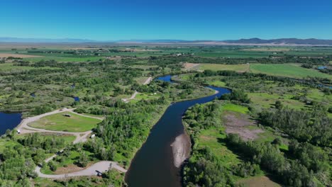 Río-Que-Fluye-A-Través-De-Campos-Verdes-En-Saint-Anthony,-Idaho,-Estados-Unidos---Toma-Aérea-De-Drones