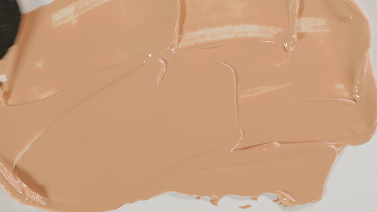 Fondotinta liquido beige cremoso spalmato su superficie bianca
