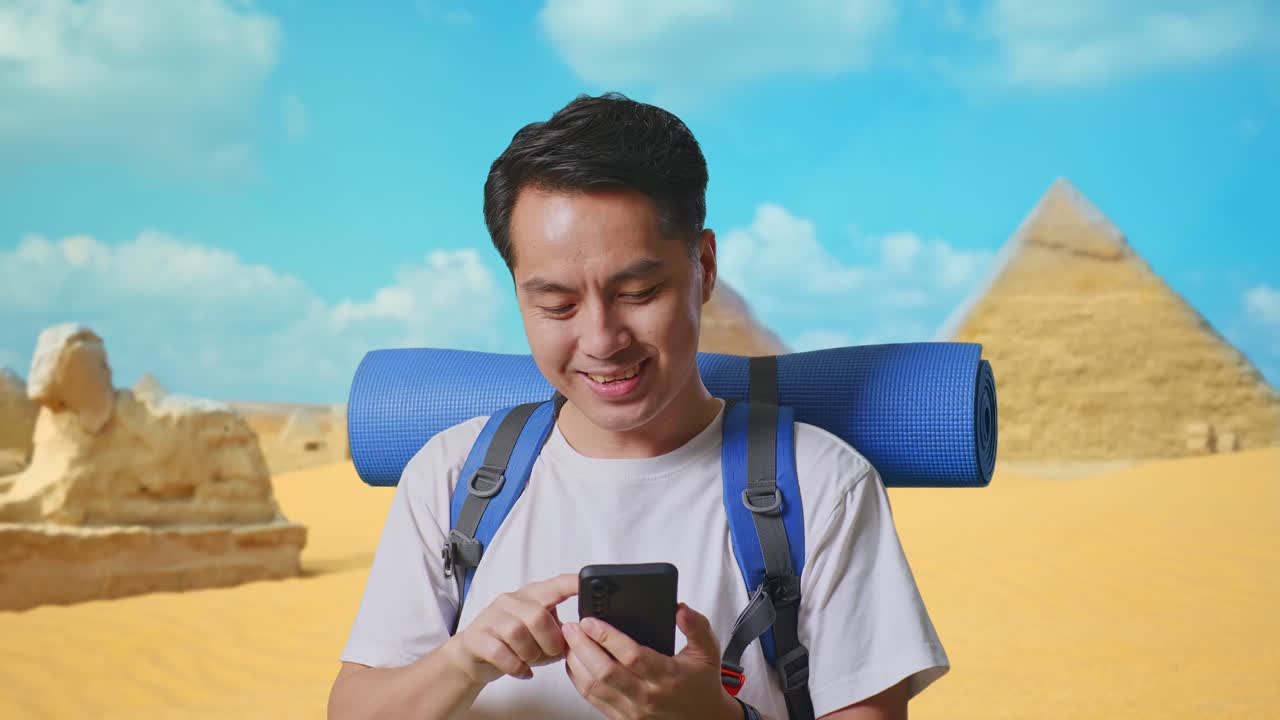Close Up Of Asian Male Hiker With Mountaineering Backpack Enjoy Using Smartphone While Traveling In Pyramid Of Giza