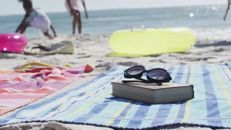 video of sunglasses, book, towels and beach equipment lying on beach