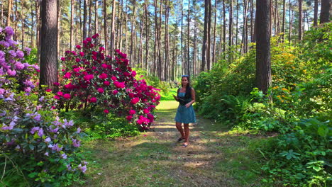 Slow-Motion-approach-of-woman-in-sundress,-in-forest-with-colourful-flowers-and-large-trees