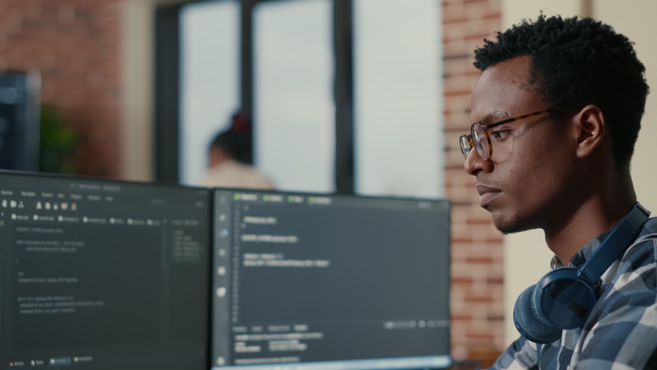 Portrait of focused software developer writing code arranging glasses sitting at desk