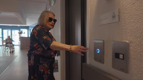 slow motion shot of an elderly woman pressing the lift button in a retirement home