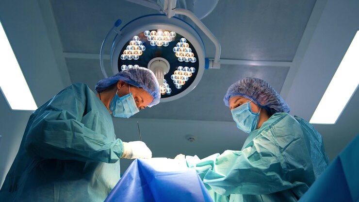 Female surgeon is holding a long metal tool. Doctor applies an instrument and scrub nurse stands opposite watching. Low angle view.
