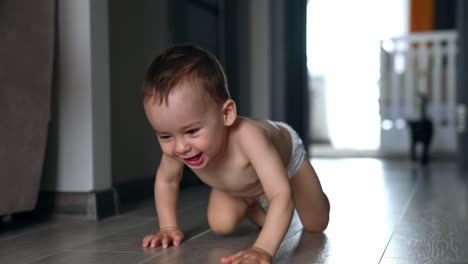 happy smiling adorable baby in diaper crawls by the room. black cat follows the child.