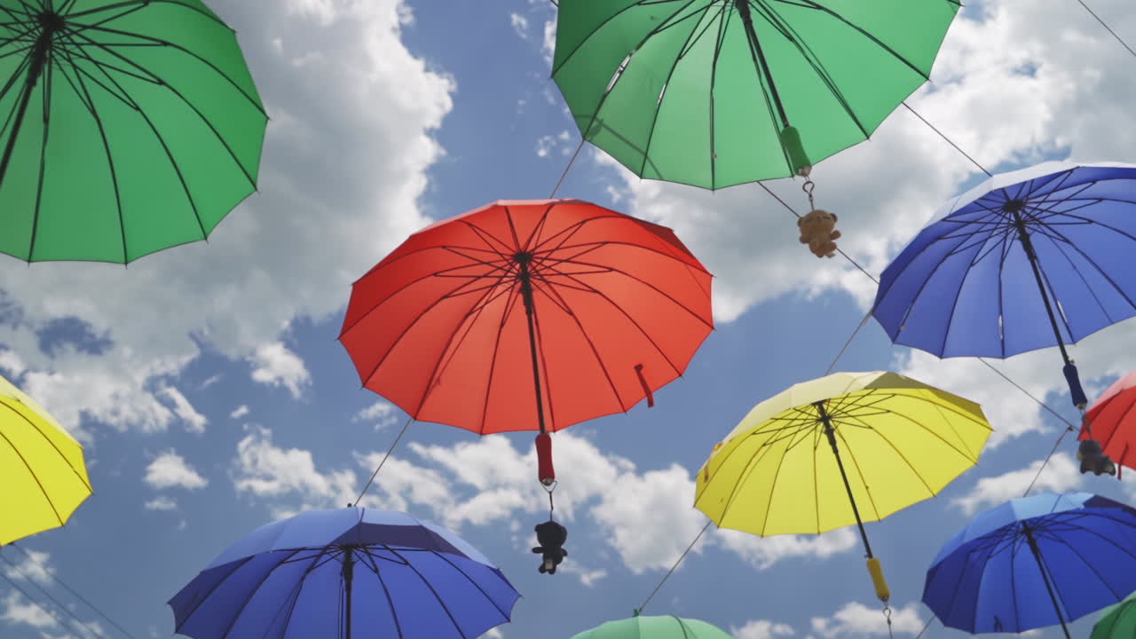 Colorful display of hanging umbrellas with attached animal charms and a blue sky background during a light breeze, medium pan right in slow motion.