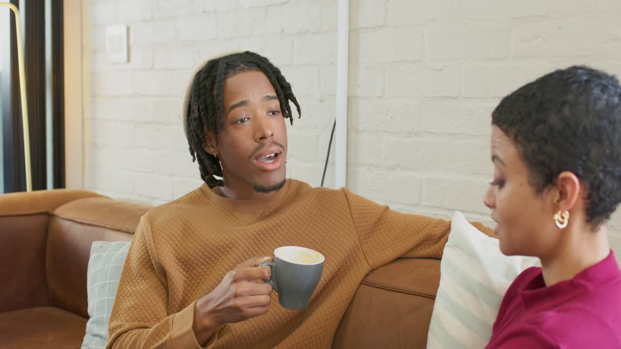 Diverse friends holding coffee mug and sharing ideas while talking in living room over couch
