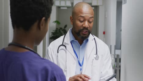 african american male and female doctors using tablet, talking at hospital