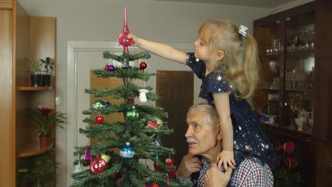 Little-child-girl-and-senior-grandfather-decorating-artificial-Christmas-tree-at-home,-slow-motion