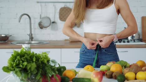 a young girl measures her waist in the kitchen near a table with fruits and vegetables