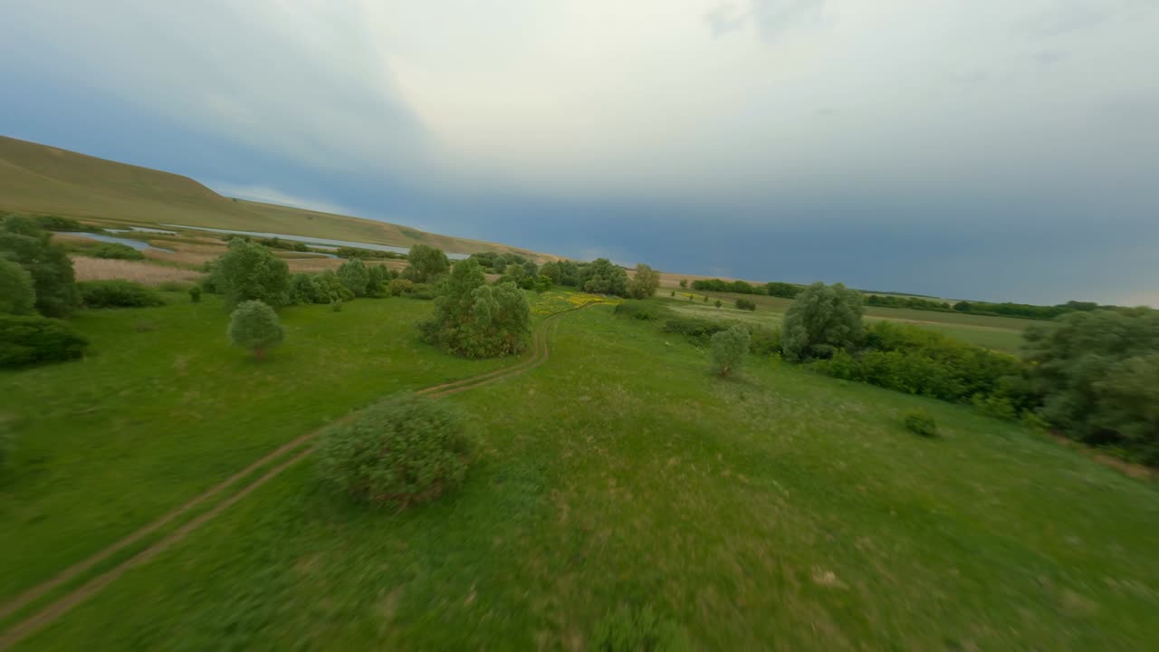 Hiking trails lead through a green valley to the river. The concept of hiking in the picturesque area. A cloudy day, the sky is reflected on the surface of the water.