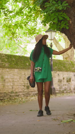 vertical video of female tourist with camera on vacation in oxford uk exploring city street walking along lamb and flag passage touching tree 3